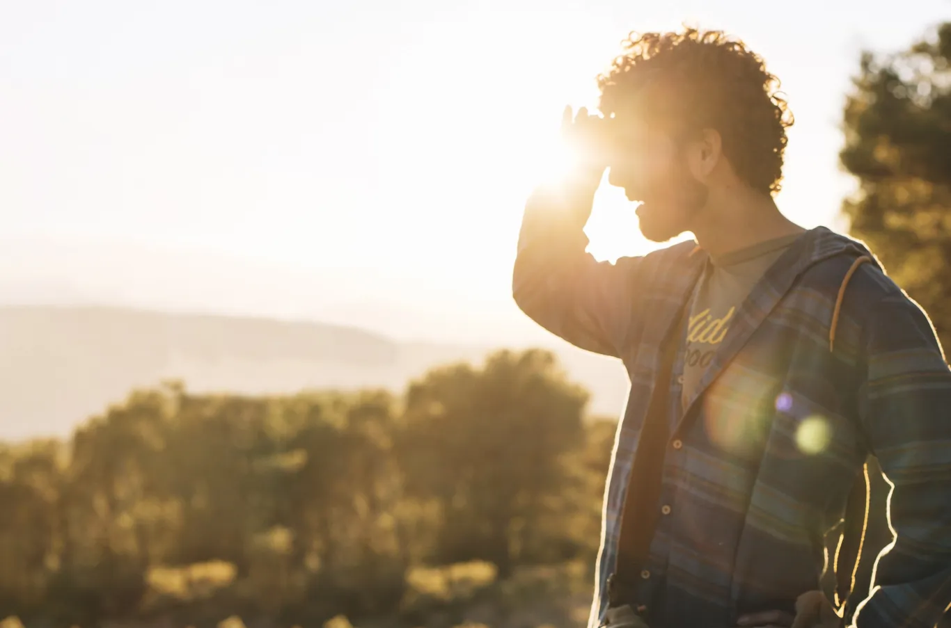 Man shielding his eyes while looking toward a bright sunset